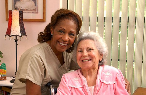 Smiling care professional with an elderly woman in a pink robe