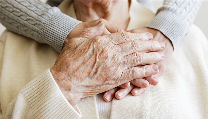 Close-up of hands gently resting over an older adult's hands